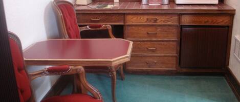 A small room with a wooden desk, a red chair, a microwave, and a telephone.