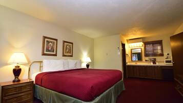 Habitación de hotel con cama, dos lámparas de noche, mesitas de noche, cómoda, espejo y una pequeña cocina.