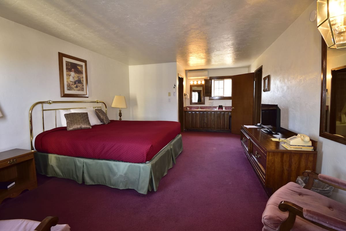 A bedroom with a large bed, a dresser, a vanity with a mirror, and a television.