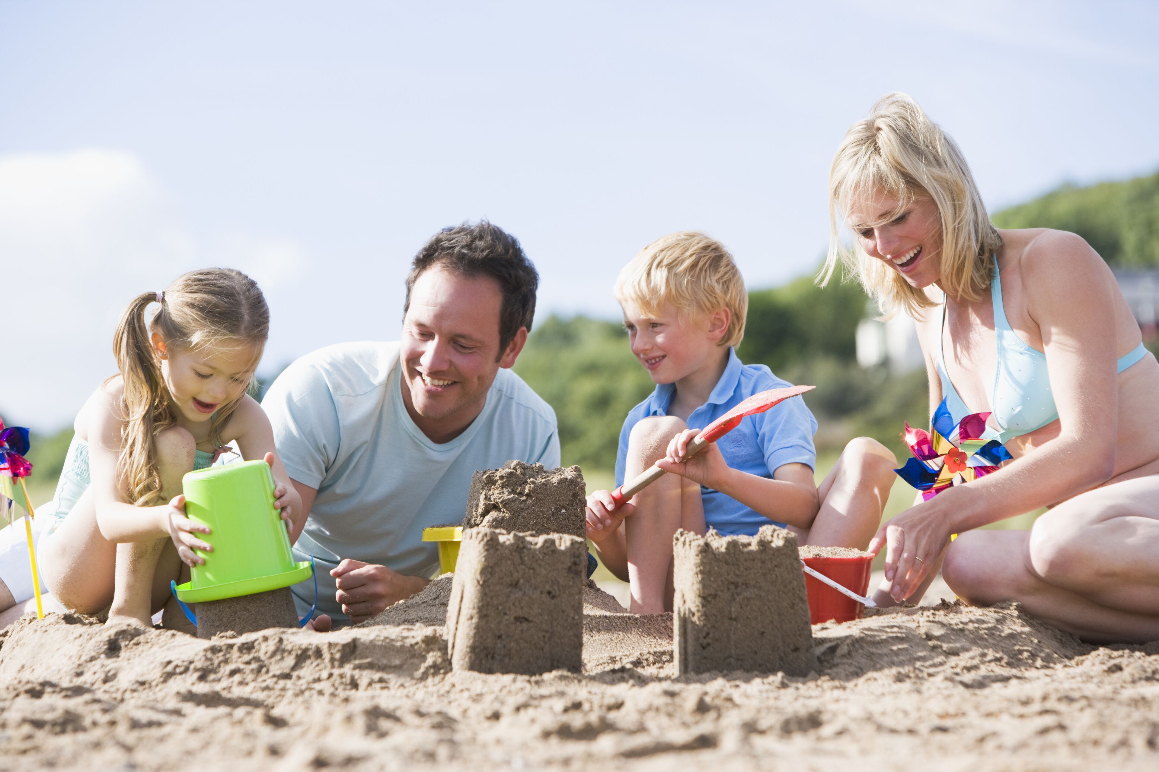 Una familia de cuatro personas construyendo castillos de arena en la playa.