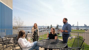 Un groupe de personnes est assis et se tient debout sur une terrasse en plein air, d’où l’on peut admirer la vue sur l’eau et le panorama de la ville.