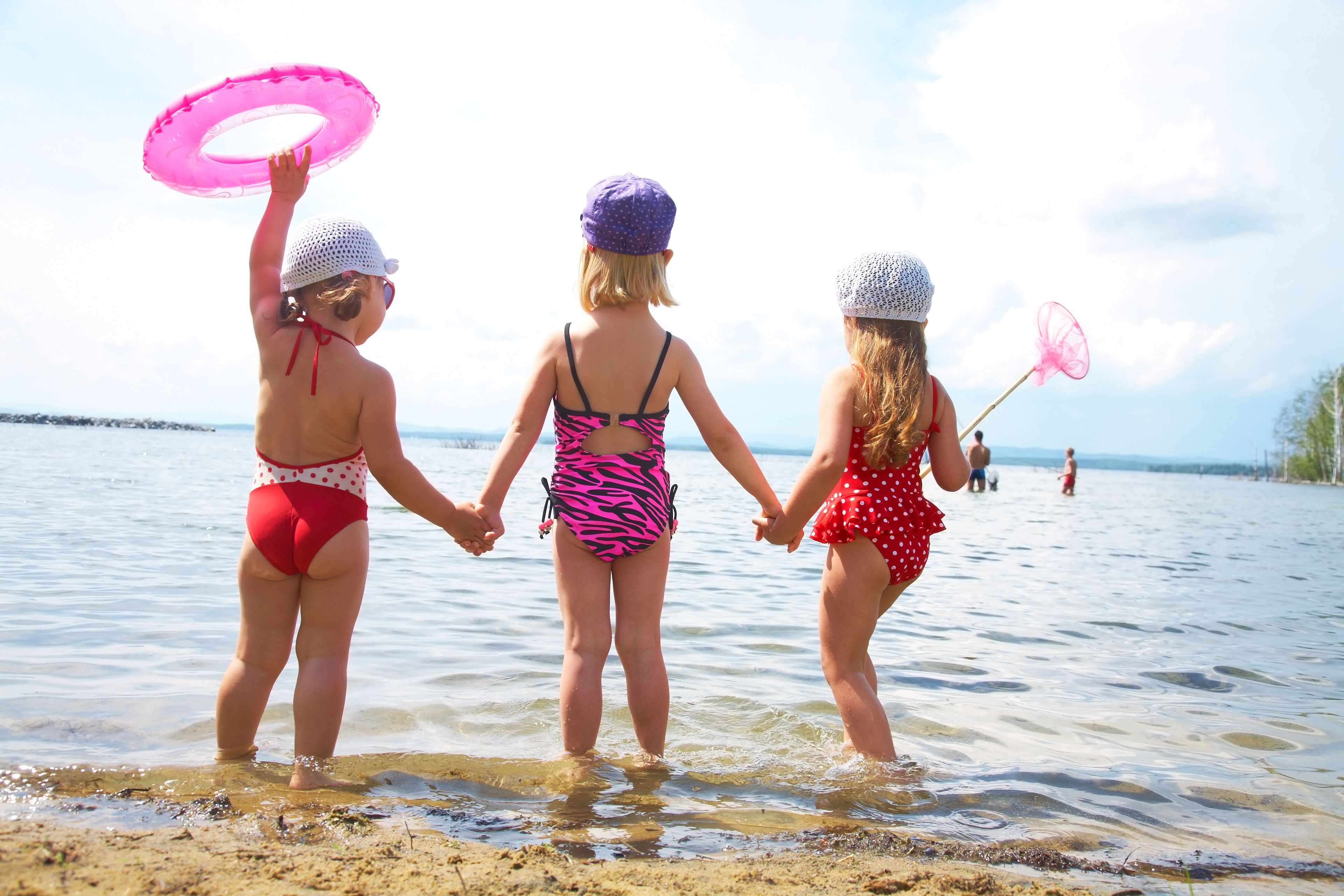 Trois enfants se tenant la main et se tenant debout dans une eau peu profonde sur une plage.