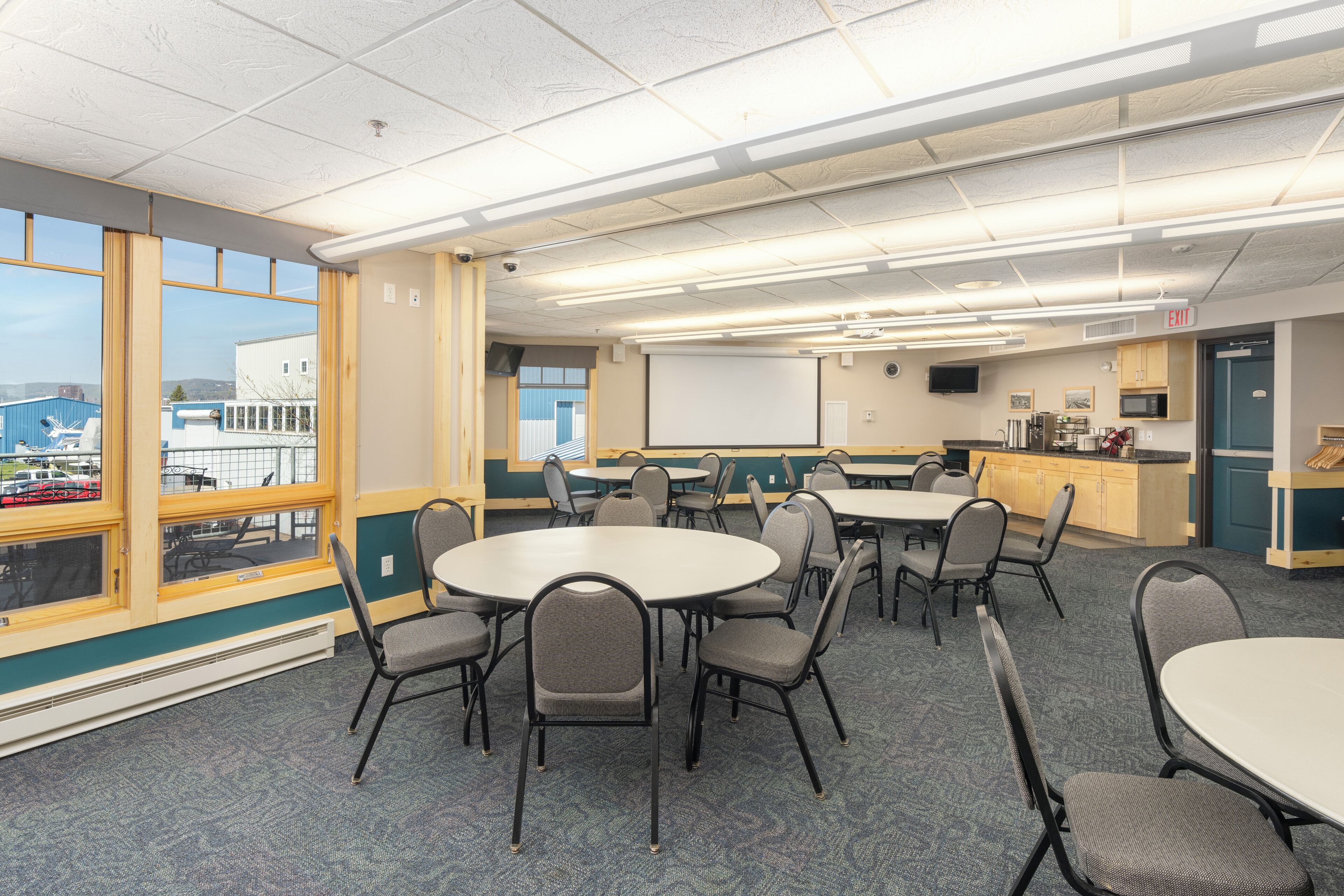 A conference room with tables and chairs, a projector screen, and a view of a building outside.