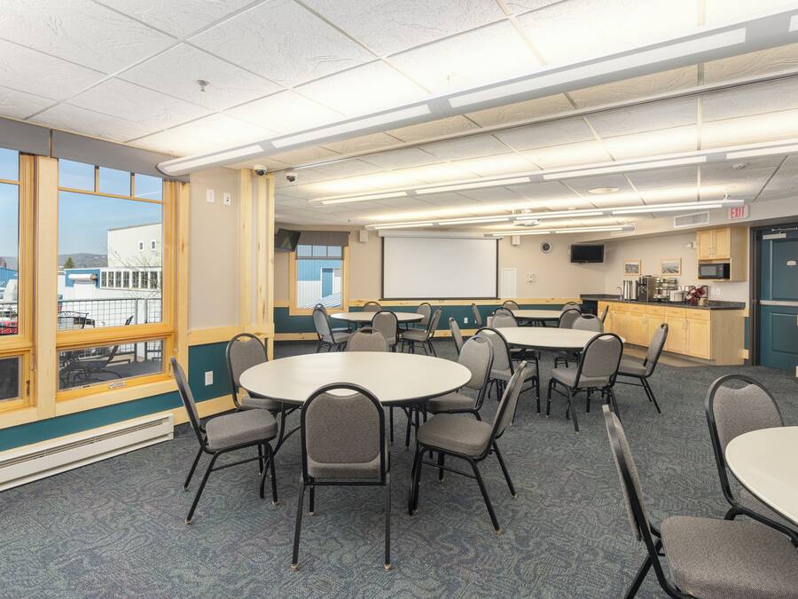 A conference room with tables and chairs, a projector screen, and a view of a building outside.