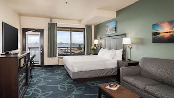 Ein Hotelzimmer mit Bett, einer Couch, einem Schreibtisch, einem Fernseher und einem Fenster mit Blick auf die Stadt.