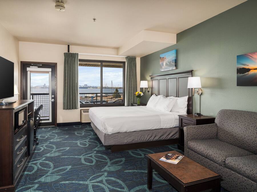 Ein Hotelzimmer mit Bett, einer Couch, einem Schreibtisch, einem Fernseher und einem Fenster mit Blick auf die Stadt.