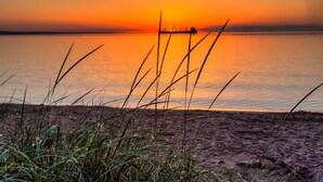 A sunset over a calm body of water with a distant boat and grassy foreground.