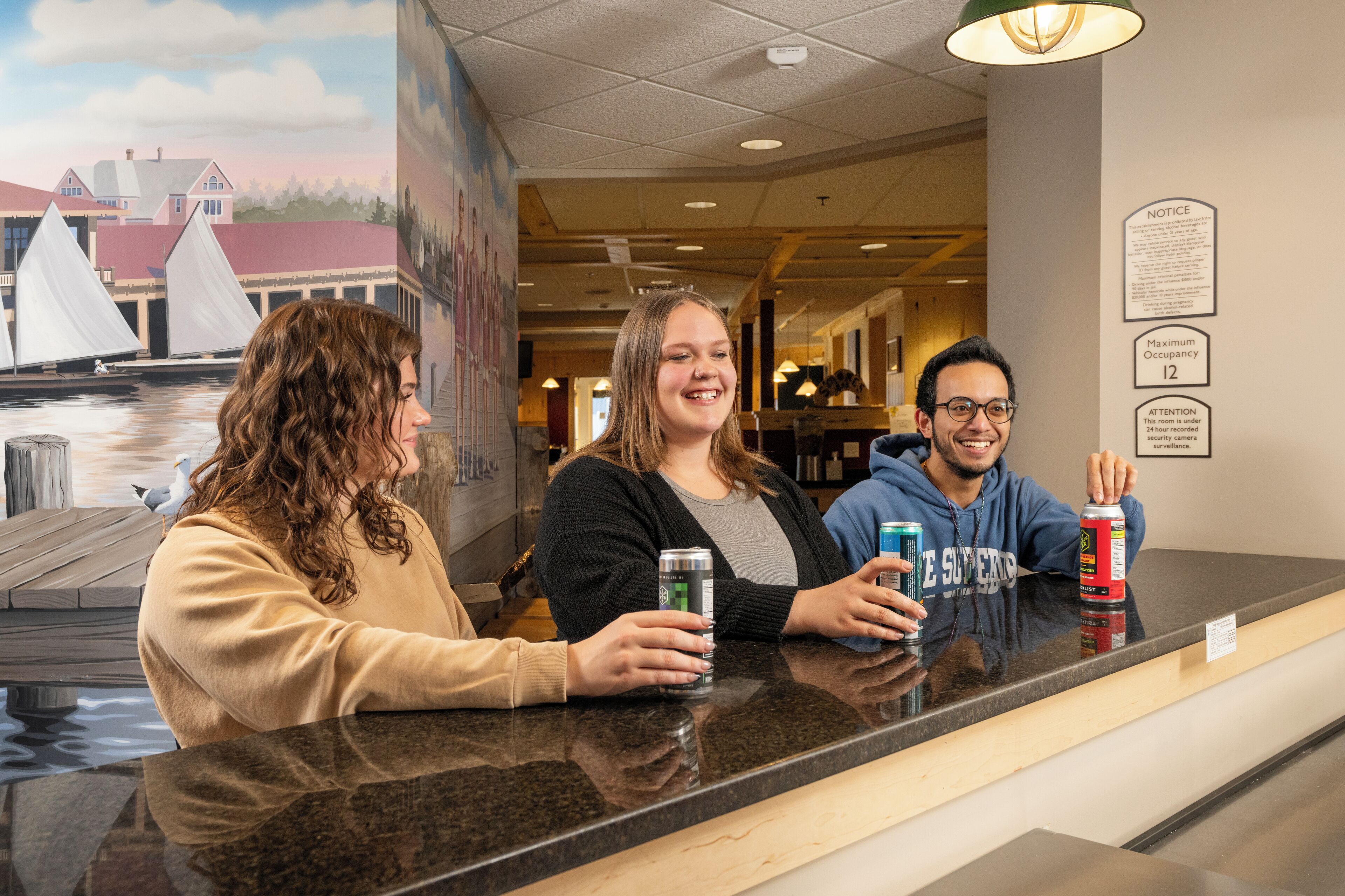 Three people at a counter with a mural of a harbor in the background.