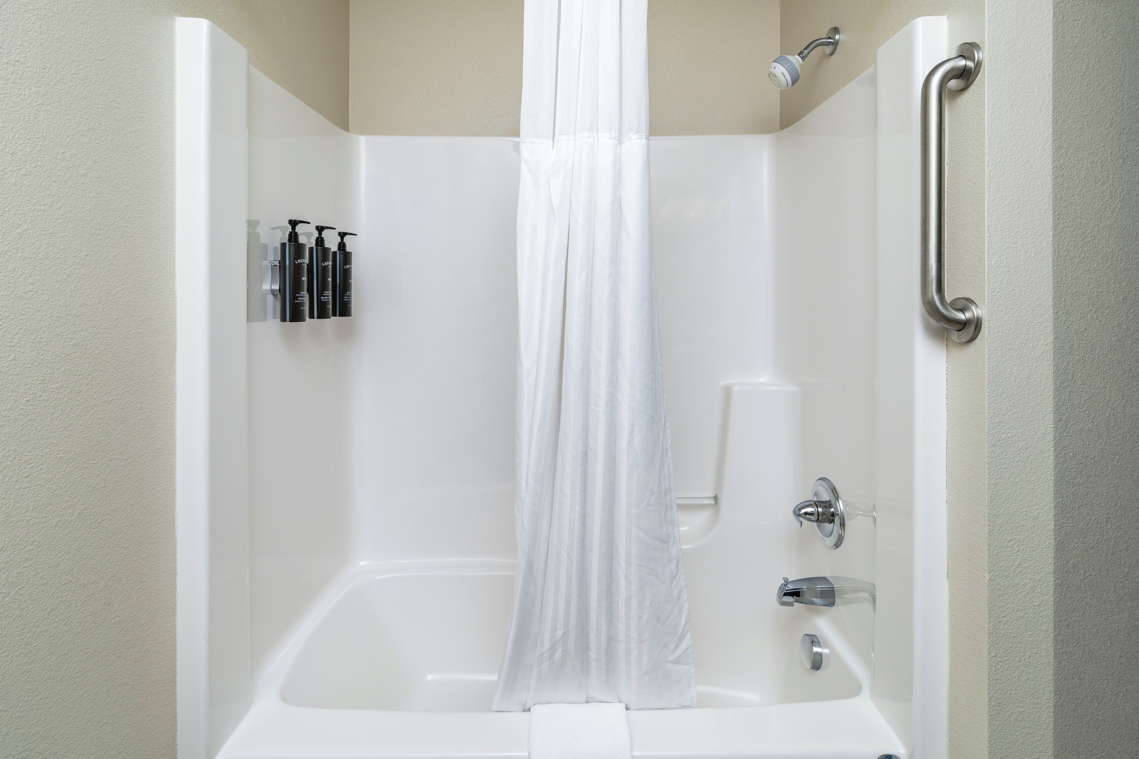 A white bathtub with a shower curtain, a handheld showerhead, a handheld shower, and a grab bar.