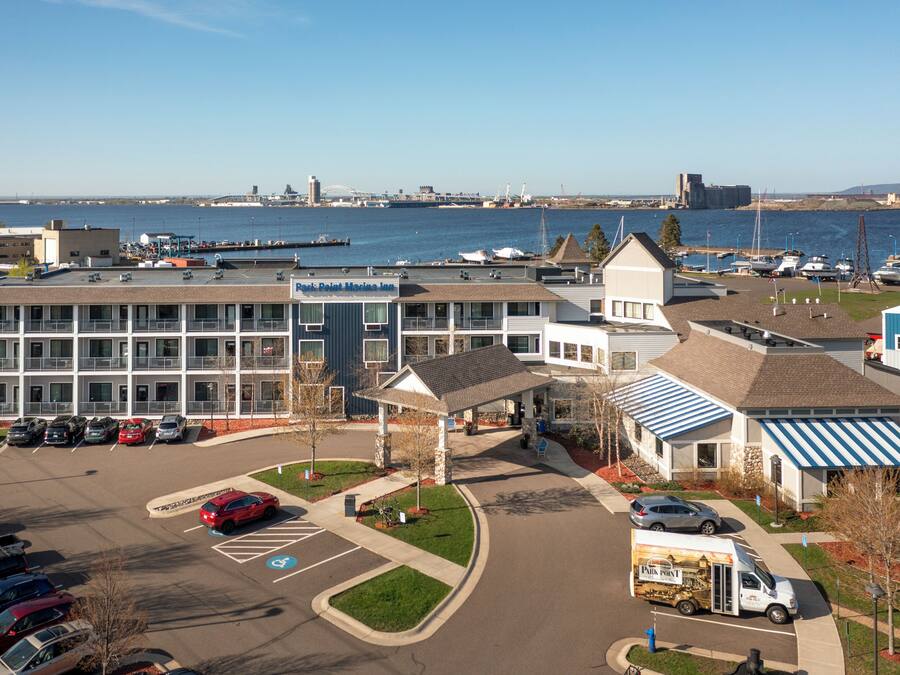 A multi-story building with a parking lot and a marina in the background.