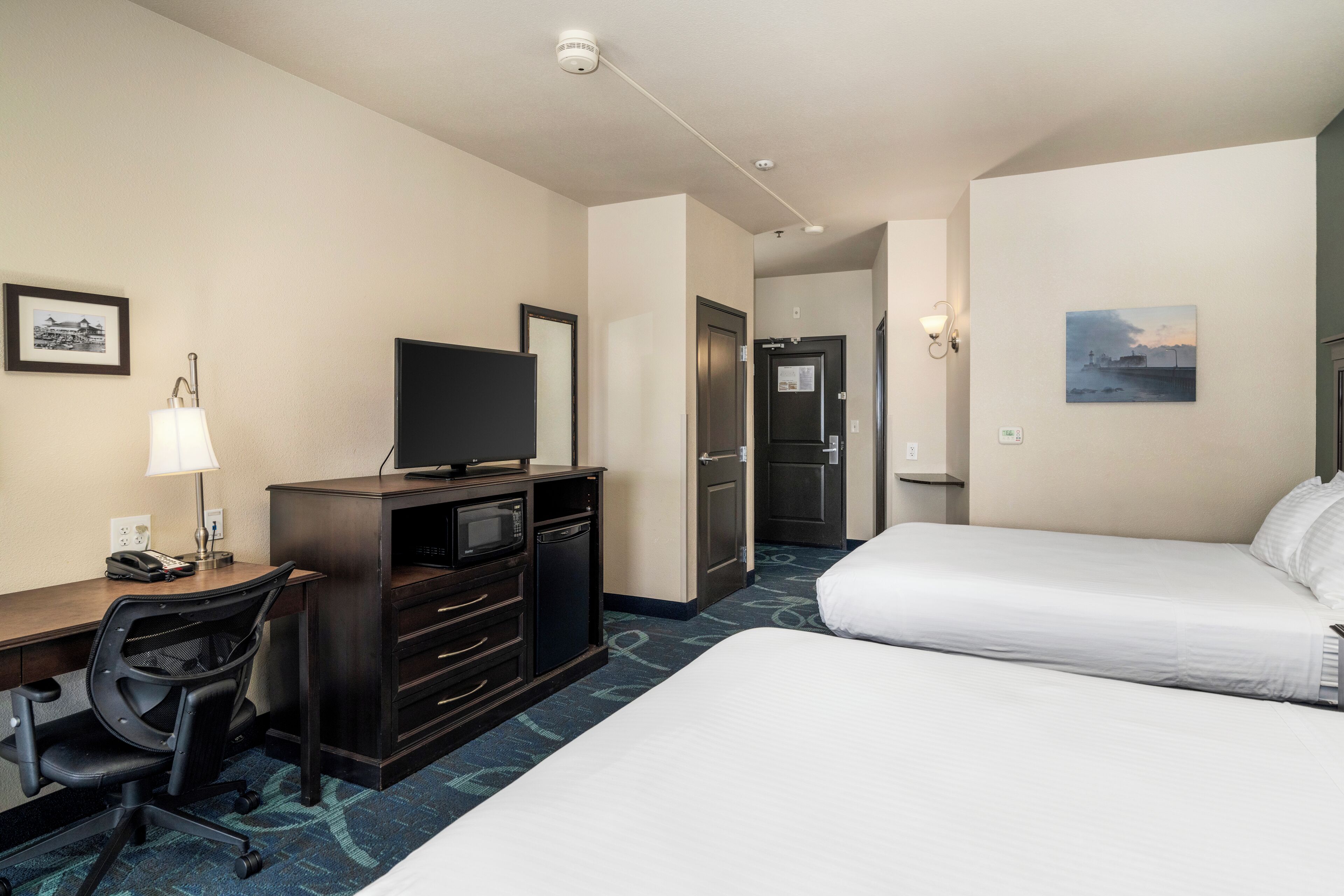 Habitación de hotel con cama, escritorio, silla, televisor y una puerta que da a otra habitación.