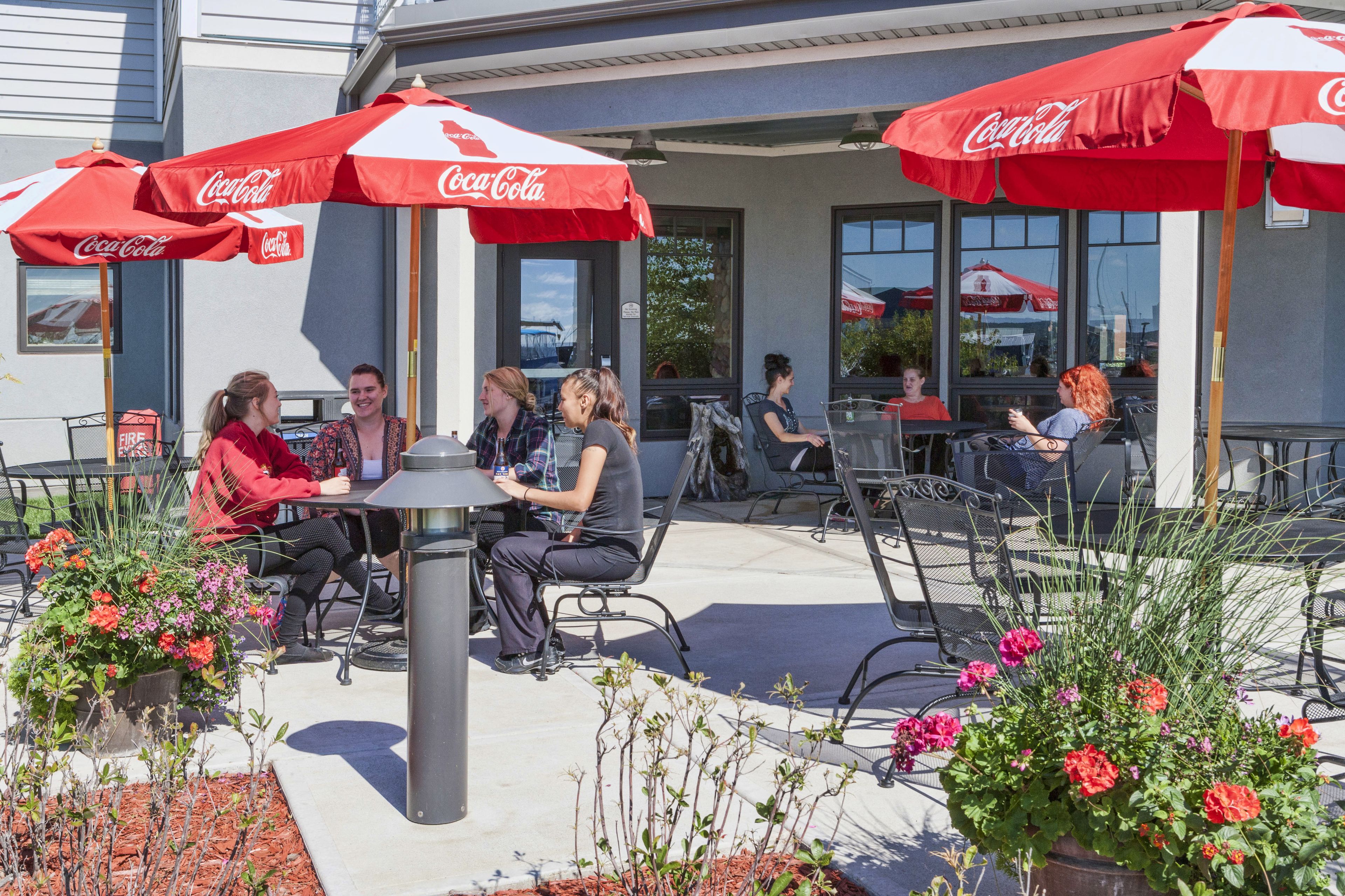 An outdoor seating area with tables and chairs, red Coca-Cola umbrellas, and potted plants.