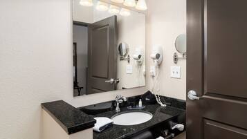 A hotel bathroom with a large mirror, a sink, a towel, and hair dryers on the wall.