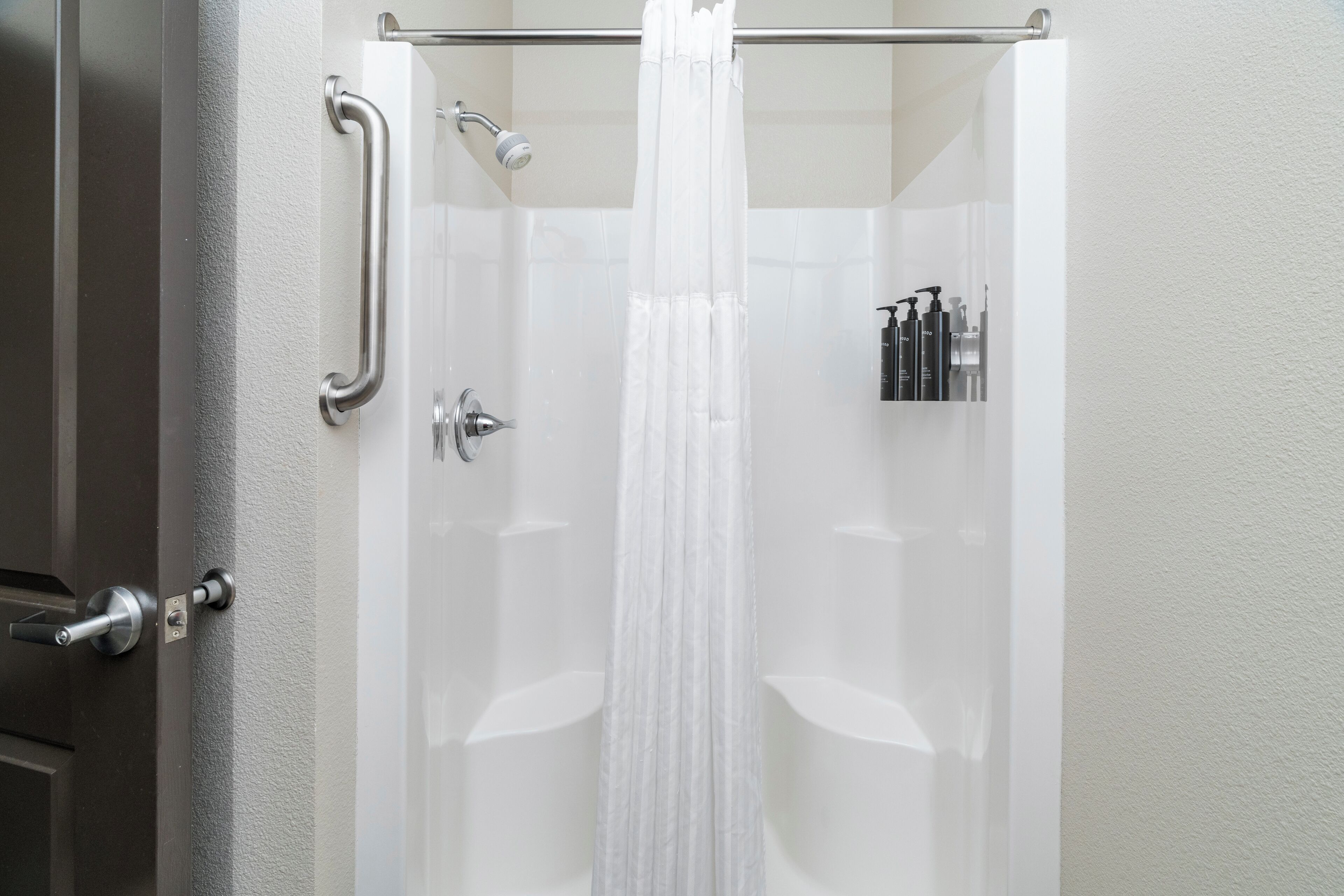 A bathroom with a shower, a handrail, and toiletries on the wall.