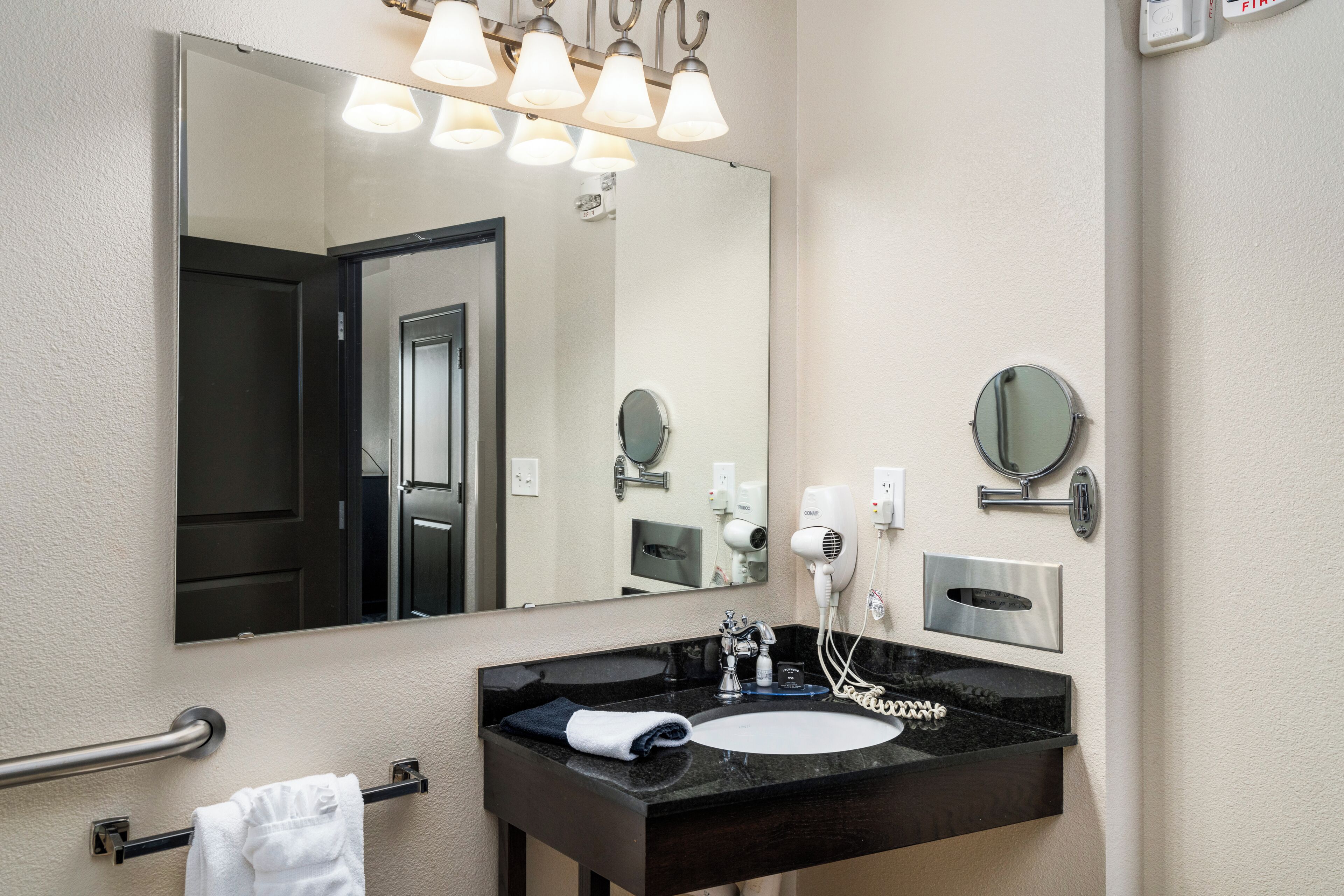 A bathroom with a large mirror, a black sink, a towel rack, and a hairdryer.