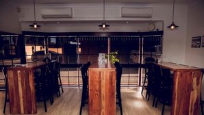 Moderni ruokailutila, jonka keskellä on suuri puinen pöytä, jonka ympärillä on tuoleja. Tilaa valaisevat suuret ikkunat, joissa on sälekaihtimet, sekä riippuvalaisimet.