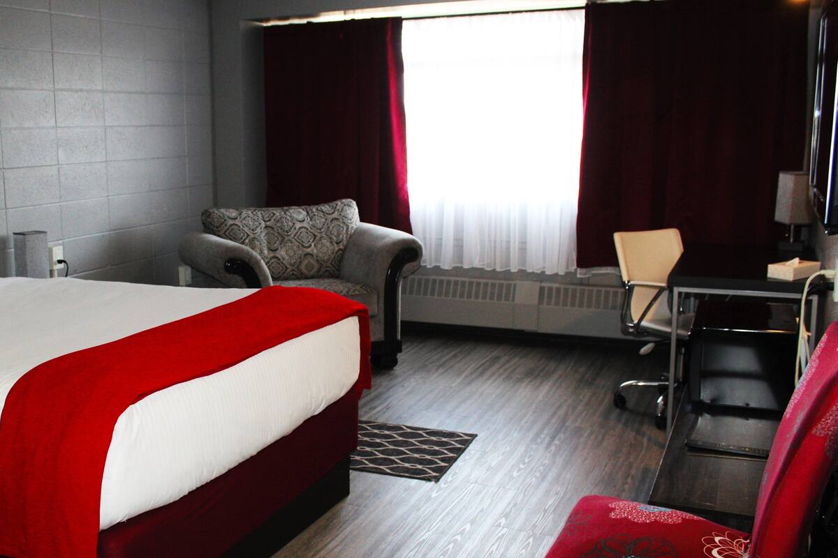 A hotel room with a large bed, a desk, a chair, and a radiator.