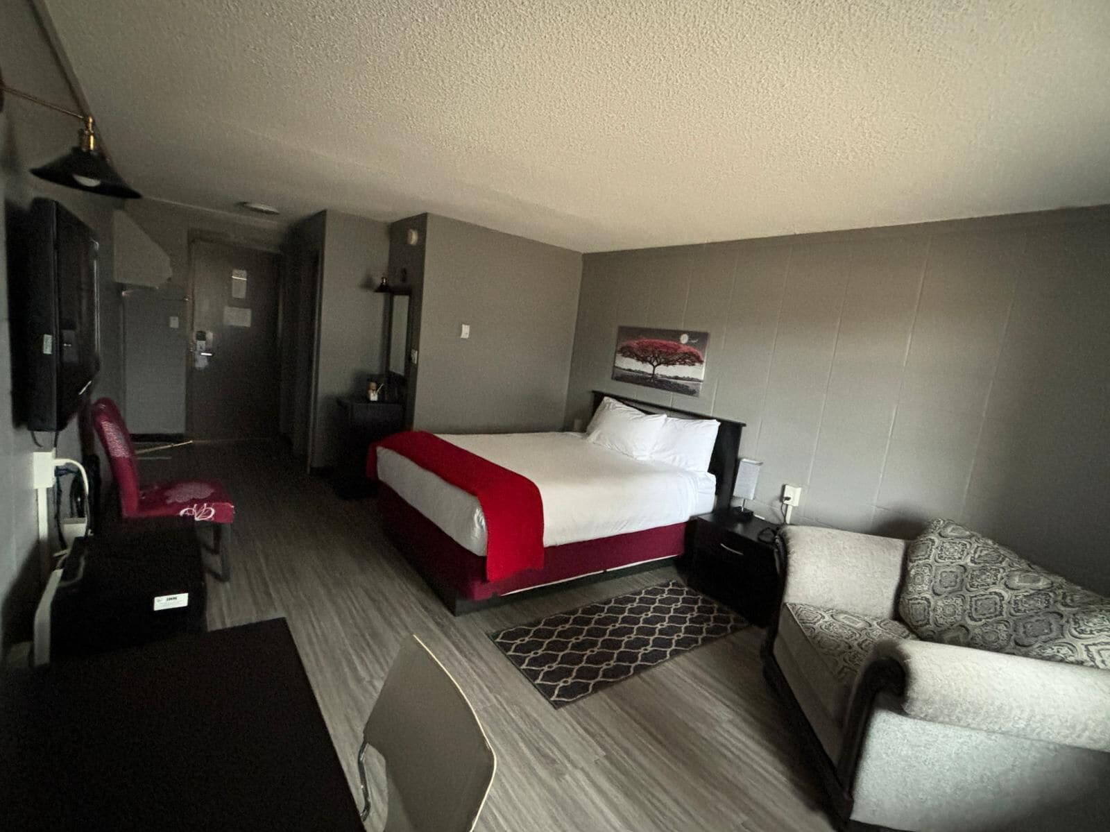 Quarto de hotel com cama, escrivaninha, cadeira, sofá, espelho e um quadro na parede.