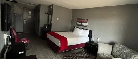 Quarto de hotel com cama, escrivaninha, cadeira, sofá, espelho e um quadro na parede.
