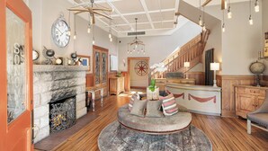 Una amplia sala de estar con chimenea de piedra, una zona de estar circular, pisos de madera y una escalera que conduce a un nivel superior.