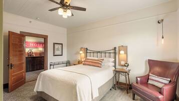 A hotel room with a bed, a chair, a nightstand, a ceiling fan, and a wall-mounted light fixture.