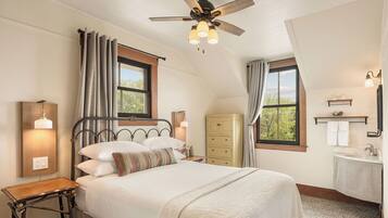 A bedroom with a bed, a ceiling fan, a nightstand, a dresser, a window, and a bathroom with a sink and mirror.