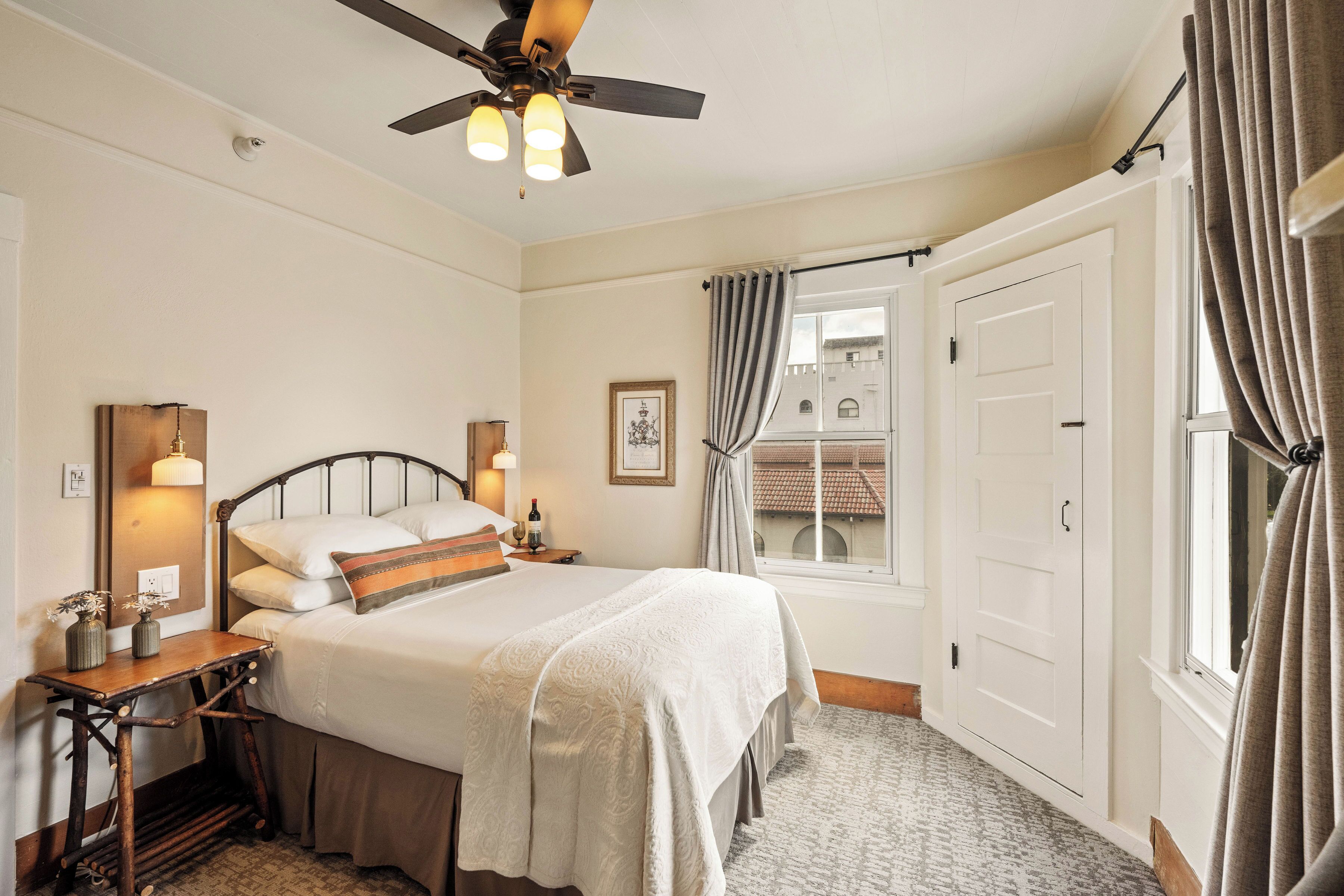 Une chambre bien rangée, avec un lit, des tables de chevet, un ventilateur de plafond et une fenêtre avec des rideaux.