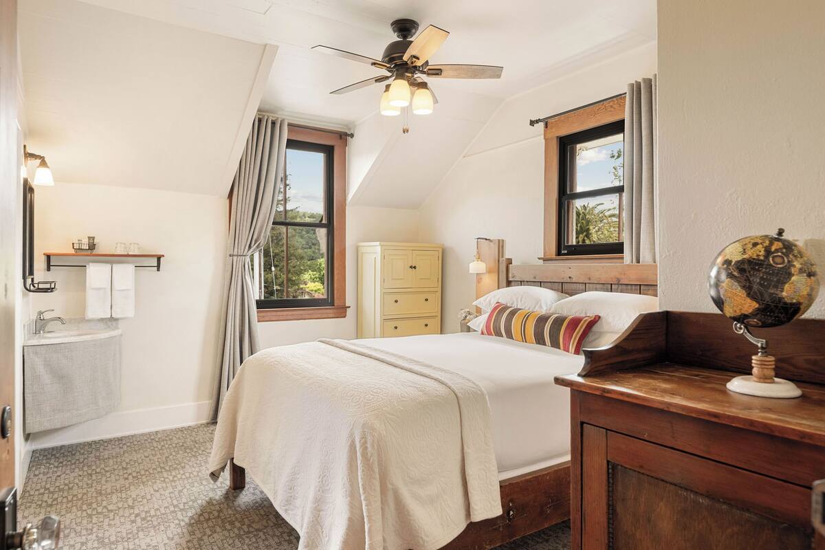 Une chambre à coucher comprenant un lit, une table de chevet, un globe terrestre, une commode, une fenêtre et un ventilateur de plafond.