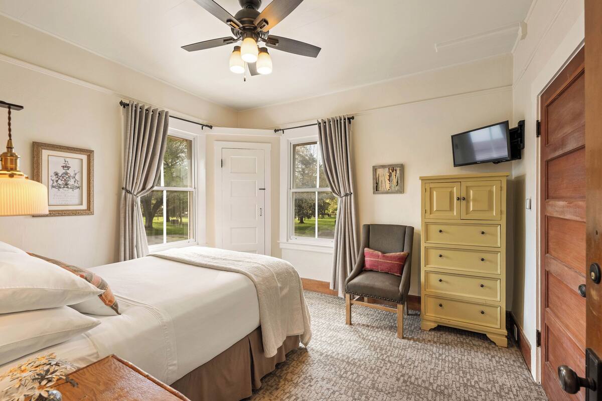 Une chambre à coucher comprenant un lit, une chaise, une commode, un téléviseur et un ventilateur de plafond.