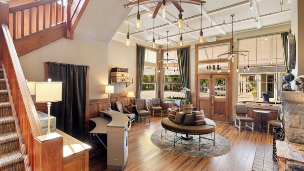 Un amplio vestíbulo de hotel con una escalera de madera, un área de estar central y ventanas grandes que ofrecen vistas al exterior.