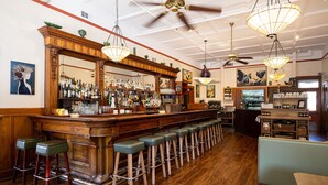 Zona de bar con taburetes de madera, barra con espejo y lámparas colgantes.