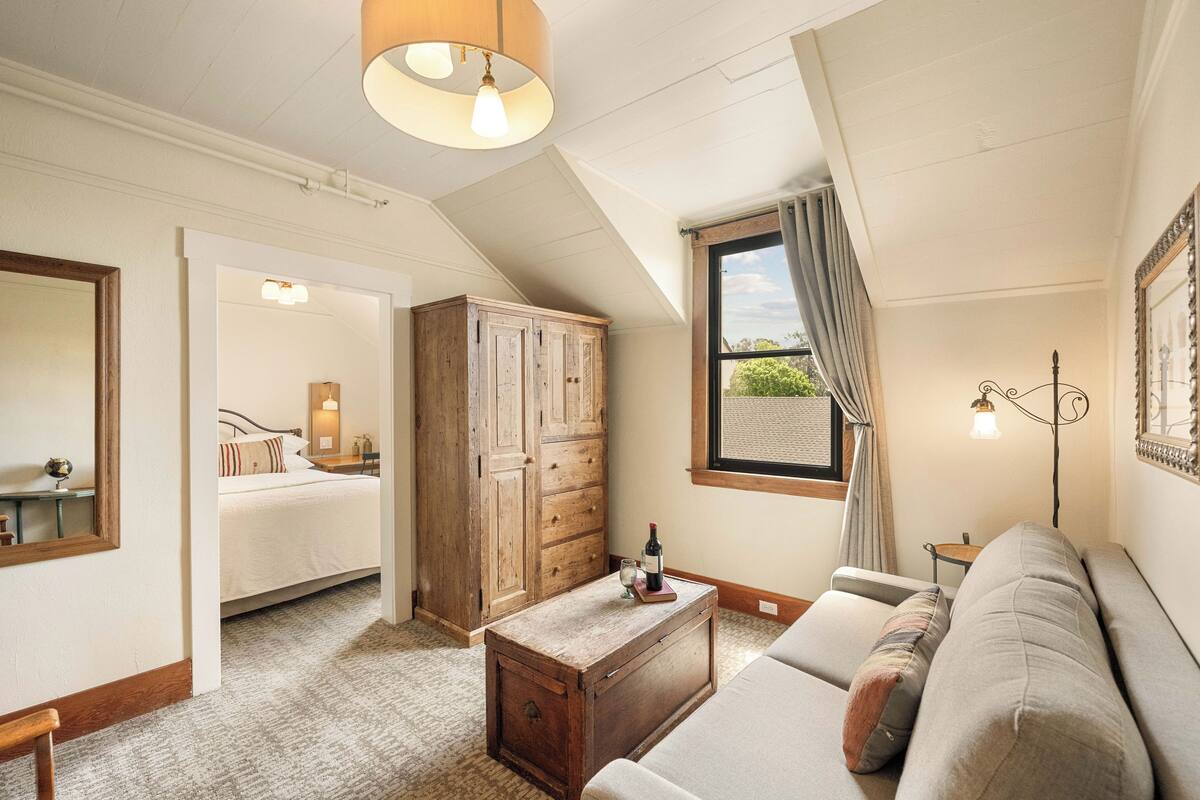 Une pièce confortable avec un lit, une commode en bois, un canapé et une fenêtre avec des rideaux.