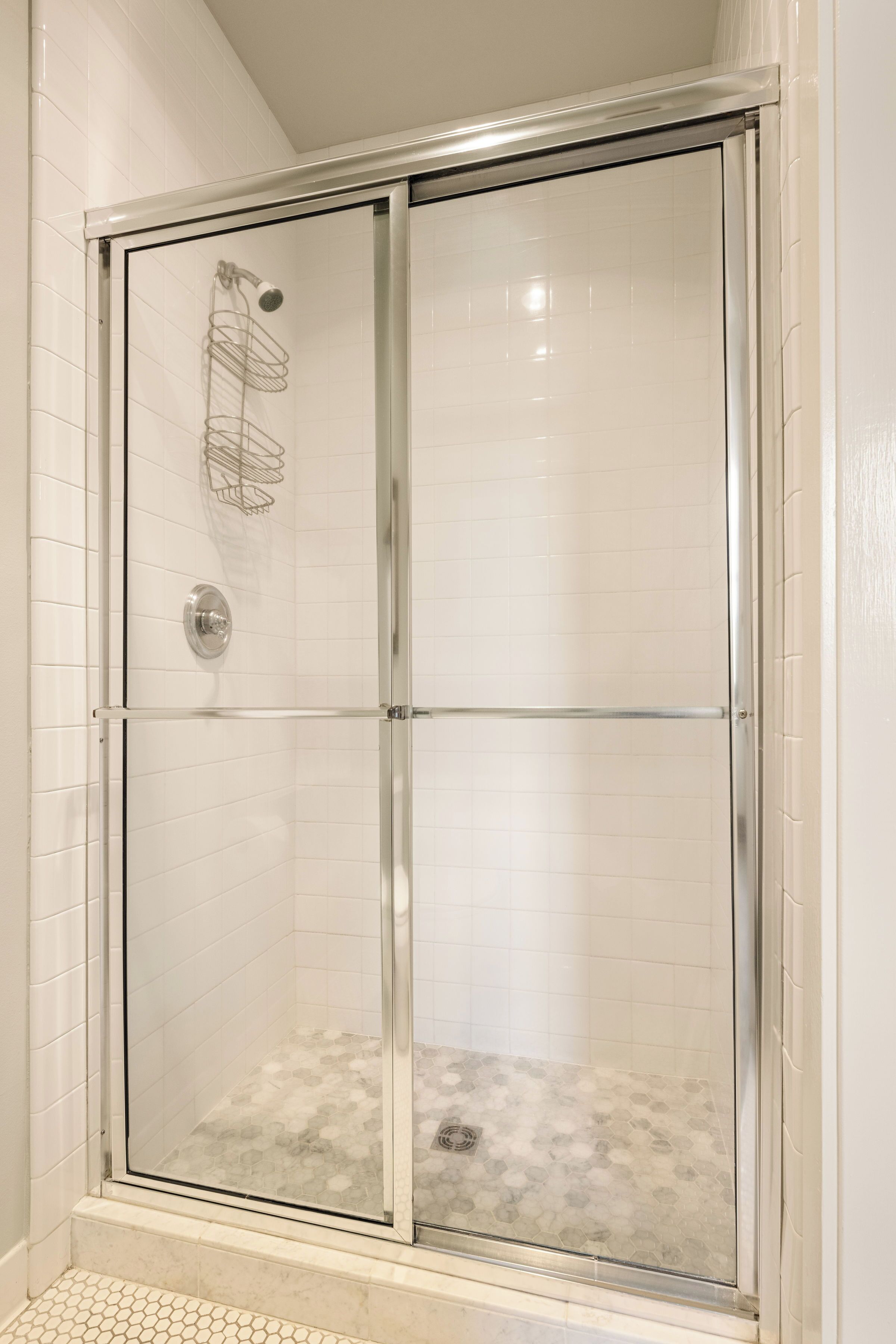 A glass-enclosed shower with a tiled floor and a metal showerhead.