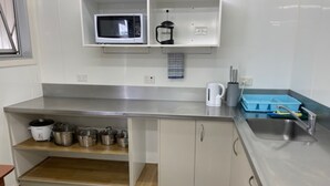Una cocina con microondas, hervidor y diferentes ollas en estantes.