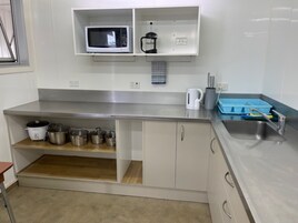 Una cocina con microondas, hervidor y diferentes ollas en estantes.