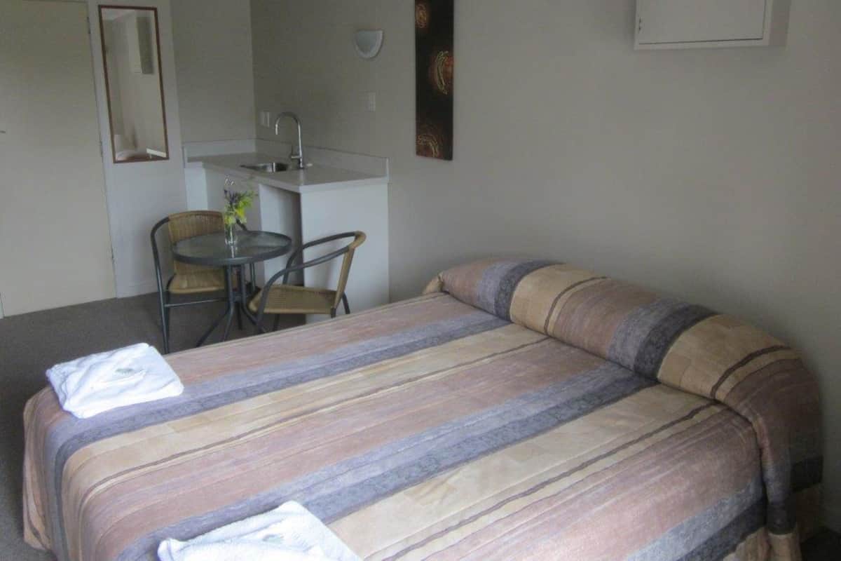 Habitación de hotel con cama, una mesita redonda con sillas, lavamanos y espejo.