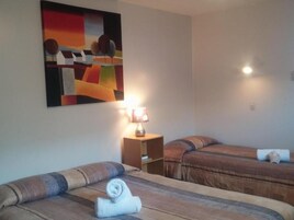Habitación de hotel con dos camas, un cuadro en la pared, una mesita de noche con lámpara y un estante pequeño.