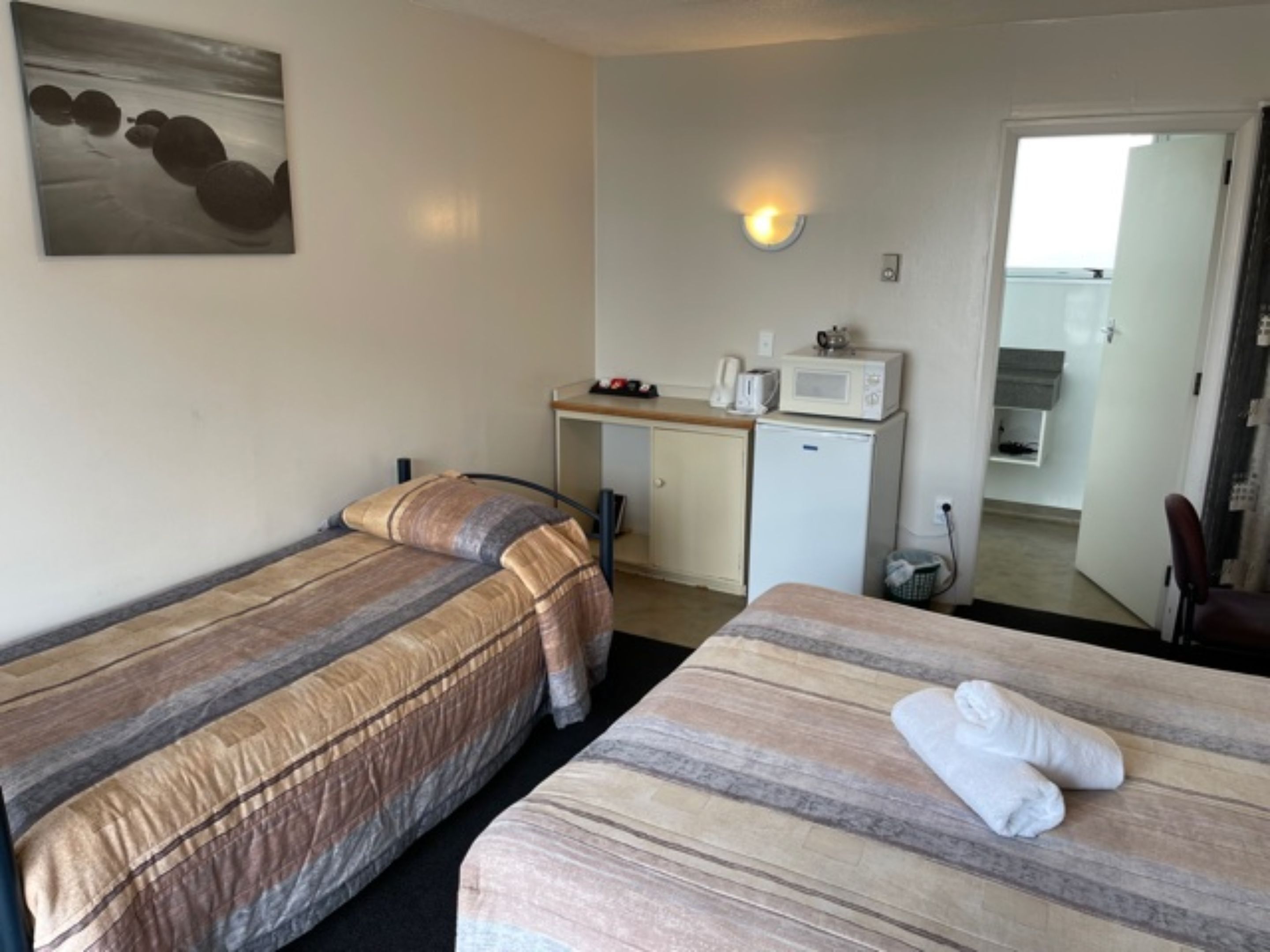 A hotel room with two beds, a kitchenette, and a bathroom visible through an open door.