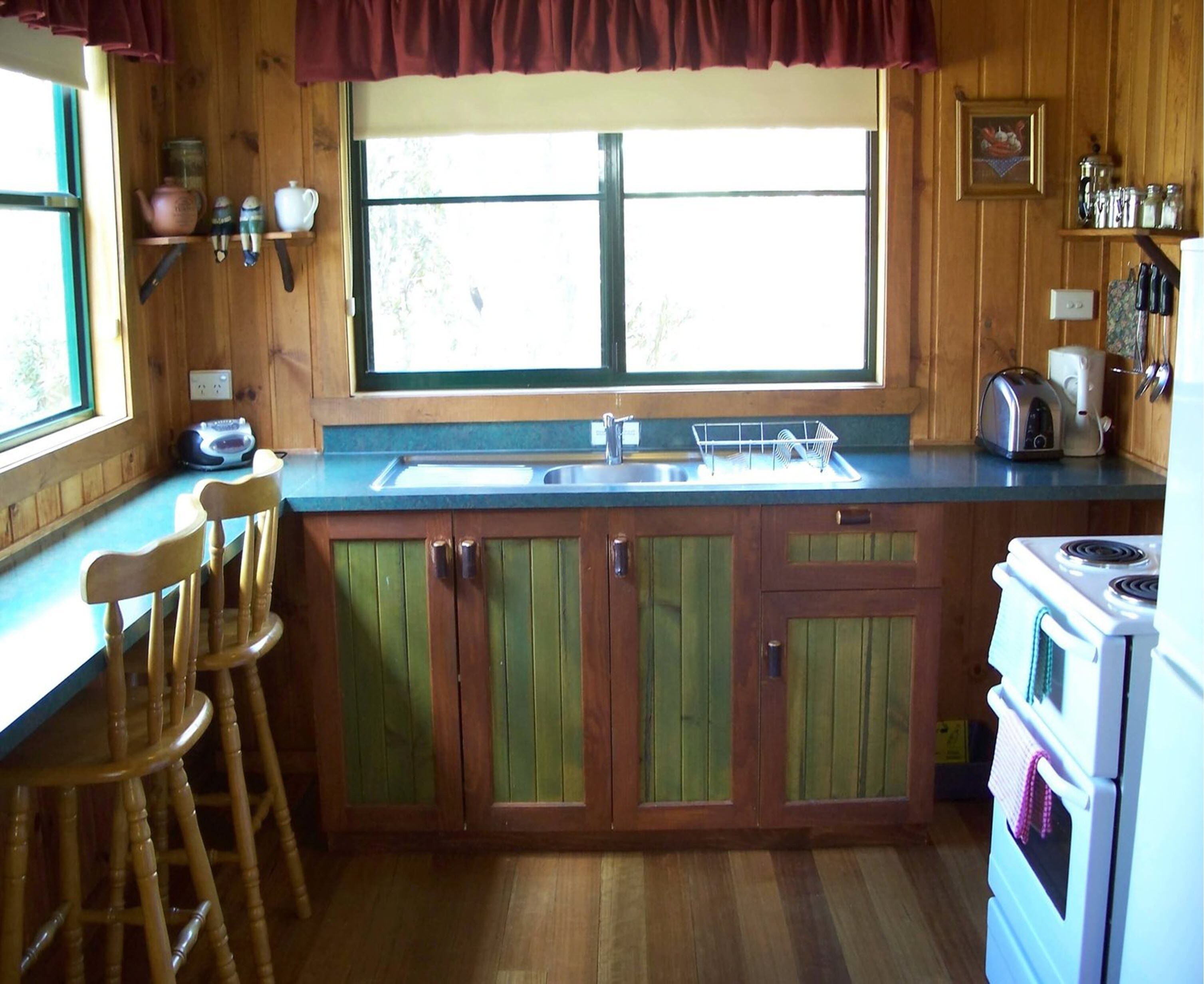 A kitchen with wooden cabinets, a window, a sink, a stove, and a bar stool.