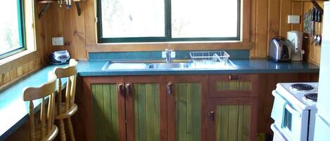 A kitchen with wooden cabinets, a window, a sink, a stove, and a bar stool.
