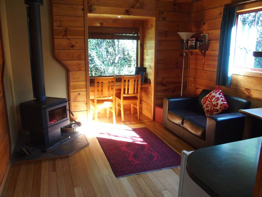 Un intérieur de chalet chaleureux avec un poêle à bois, un canapé, une table à manger et une vue sur l’extérieur.
