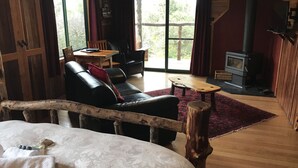 A cozy room with a bed, a wooden bench, a sofa, a small table, and a fireplace. - Cradle Highlander (Cradle Mountain)