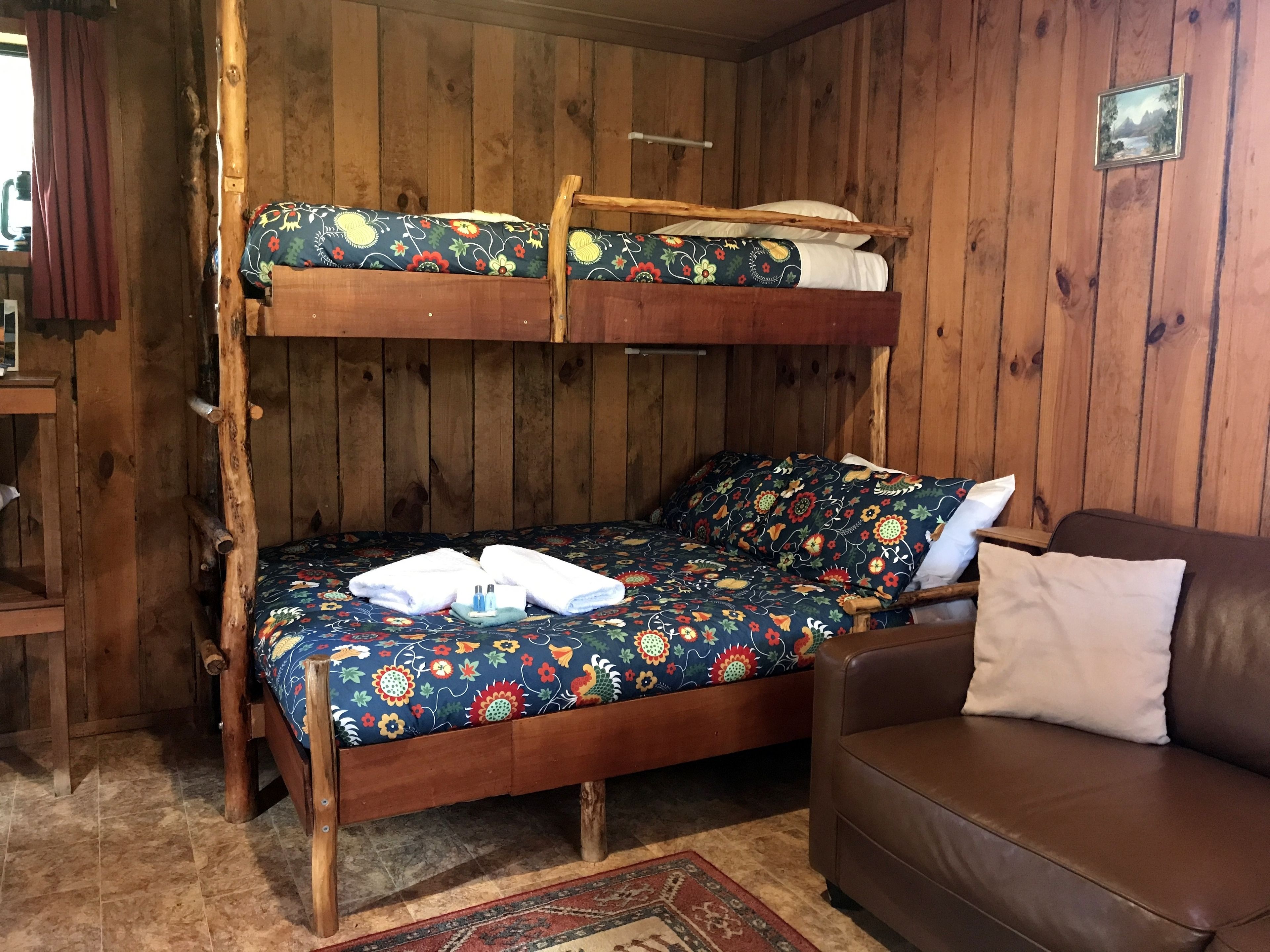 Un letto a castello in legno con biancheria da letto floreale, un divano in pelle marrone e un piccolo tappeto.