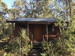 A rustic wooden building with a corrugated metal roof, surrounded by dense foliage. - Cradle Highlander (Cradle Mountain)