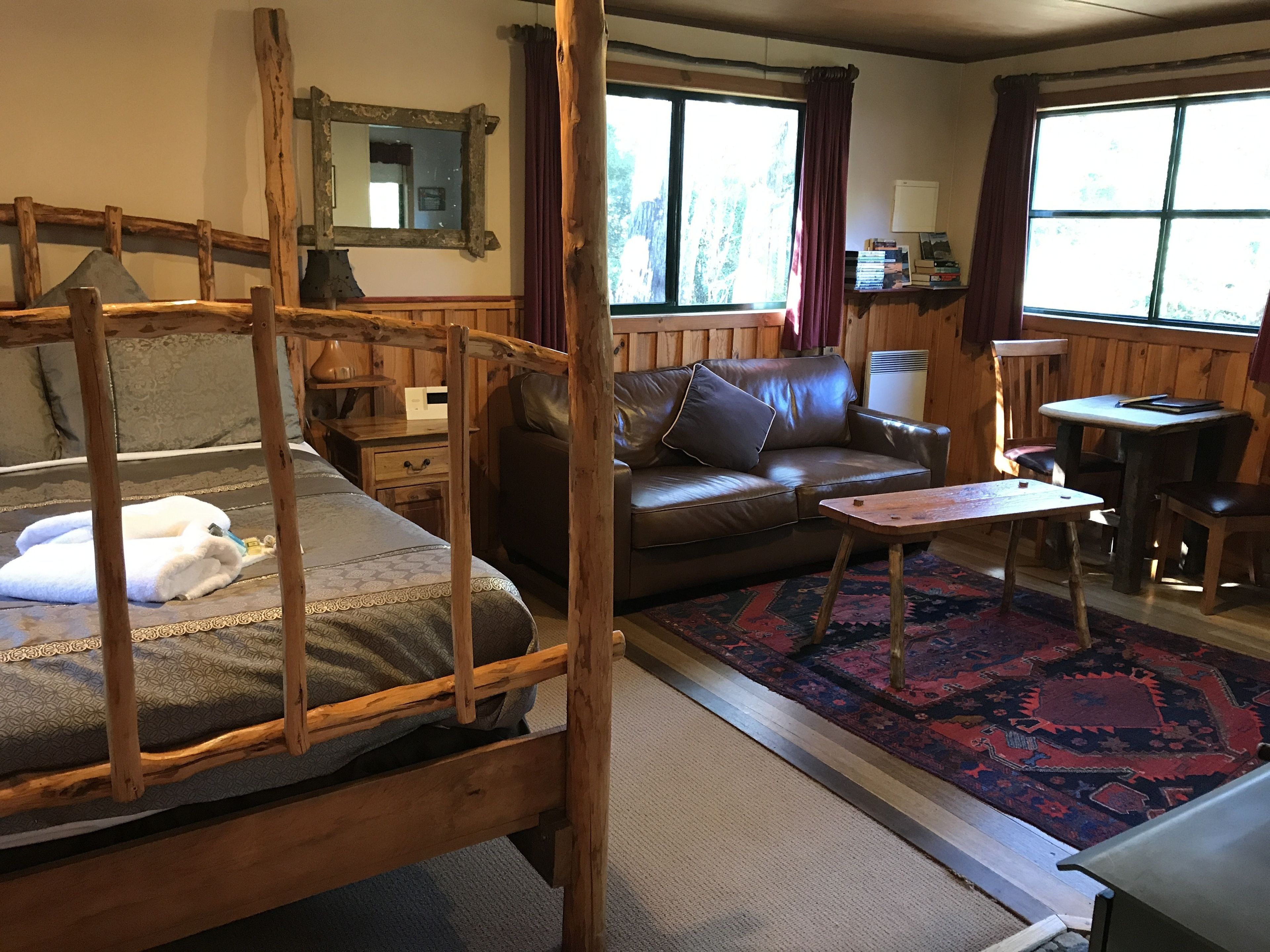 A cozy room with a wooden bunk bed, a leather sofa, a small table, and a patterned rug.