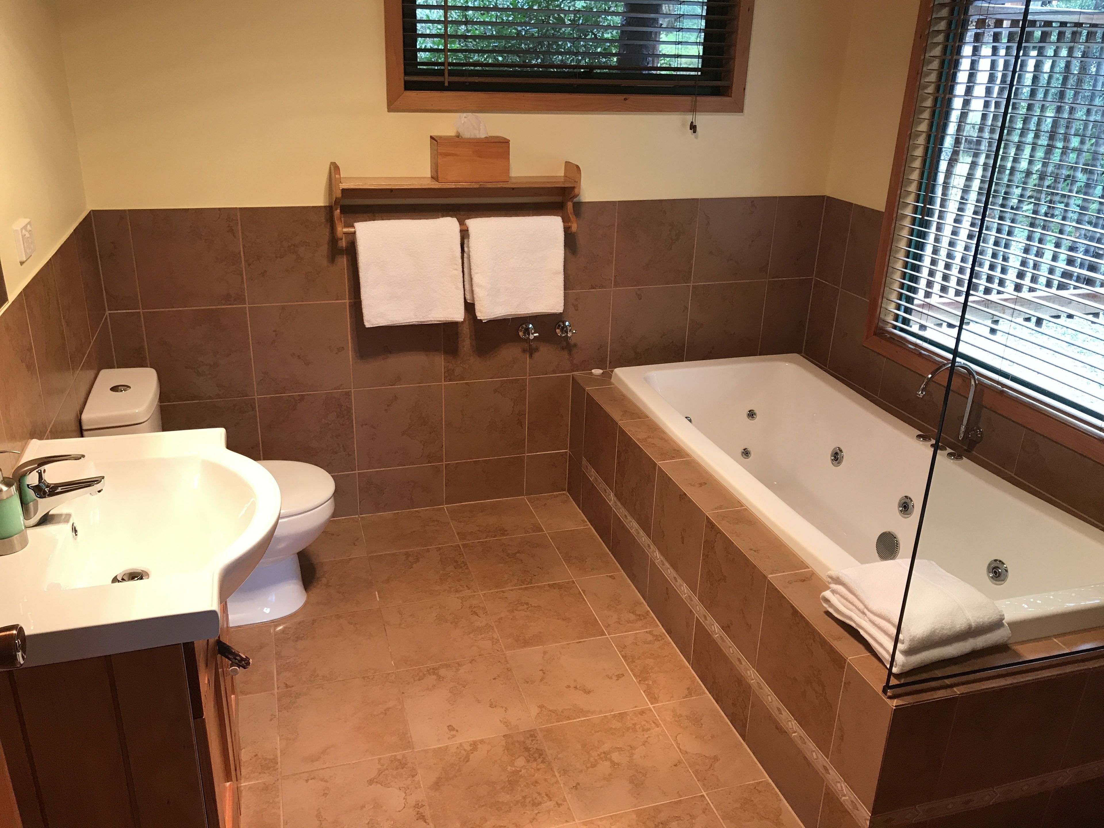 Un baño con bañera, inodoro, lavabo y una ventana con persianas.