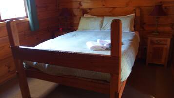 Una cama de madera en una habitación con ventana, mesita de noche y lámpara.