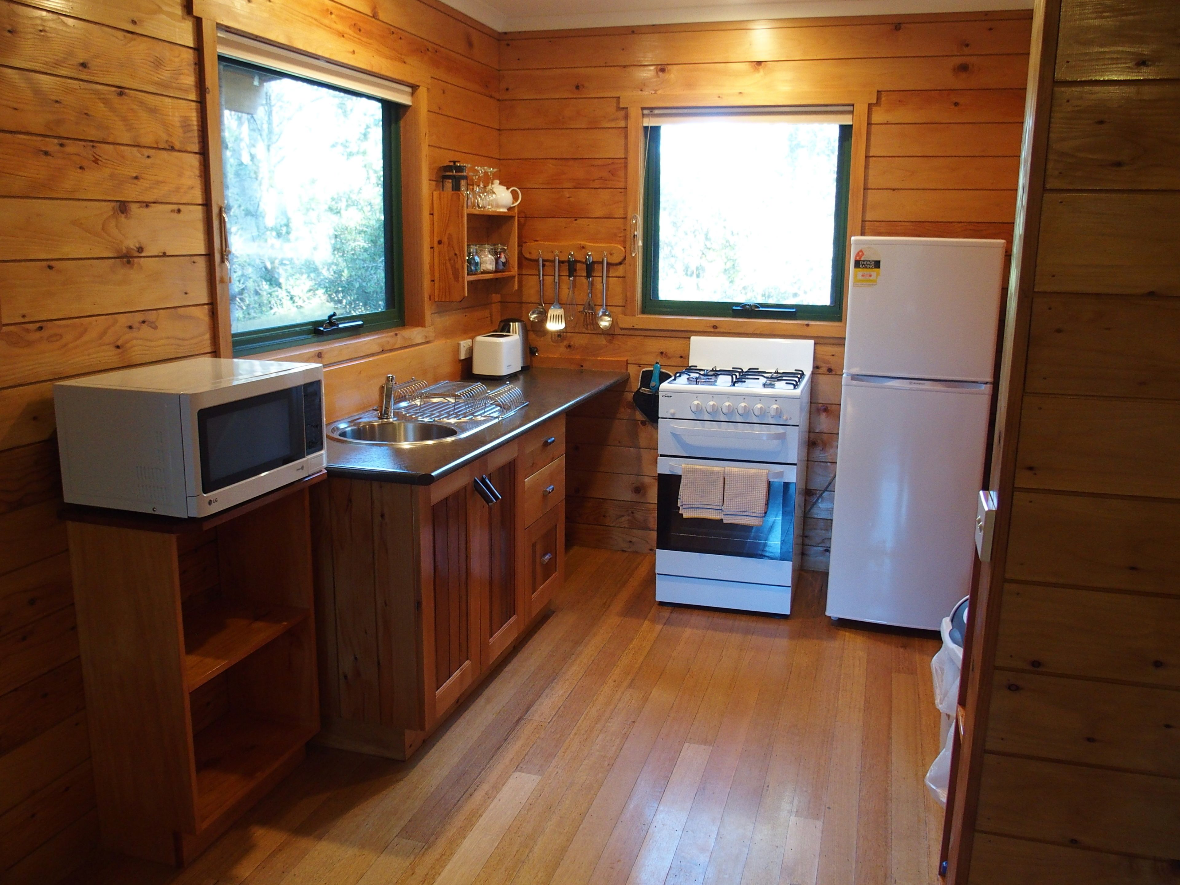 Une cuisine de taille réduite avec des murs en bois, un four à micro-ondes, une cuisinière et un réfrigérateur.