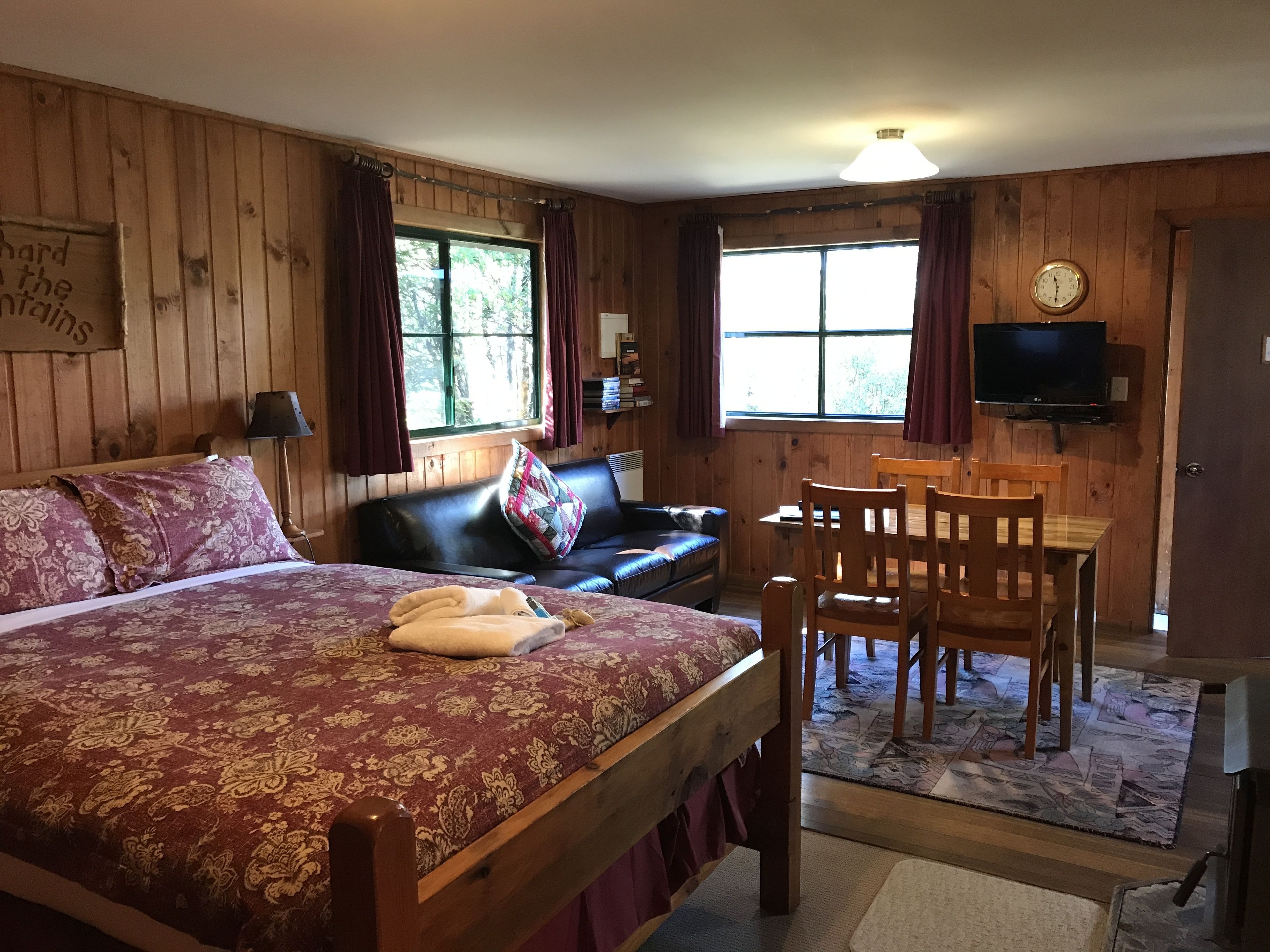 A wooden room with a bed, a sofa, a TV, and a table.