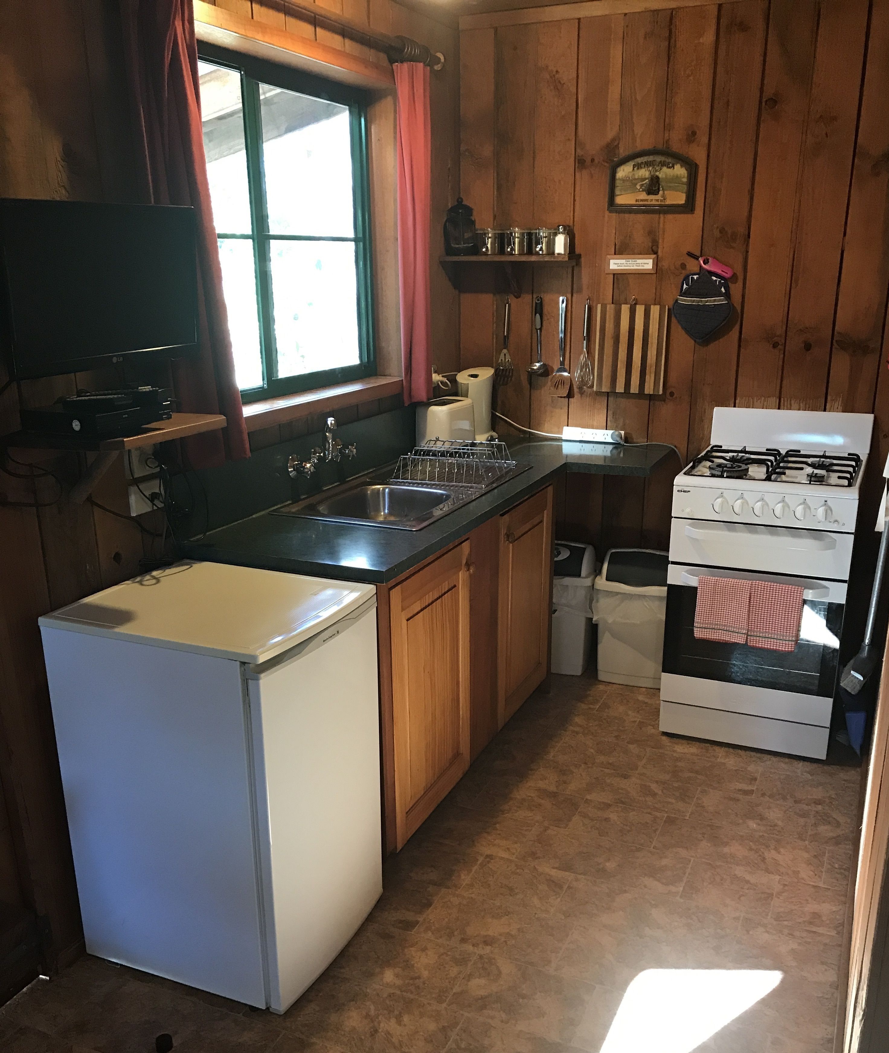 A compact kitchen with a refrigerator, stove, sink, and wooden cabinets.